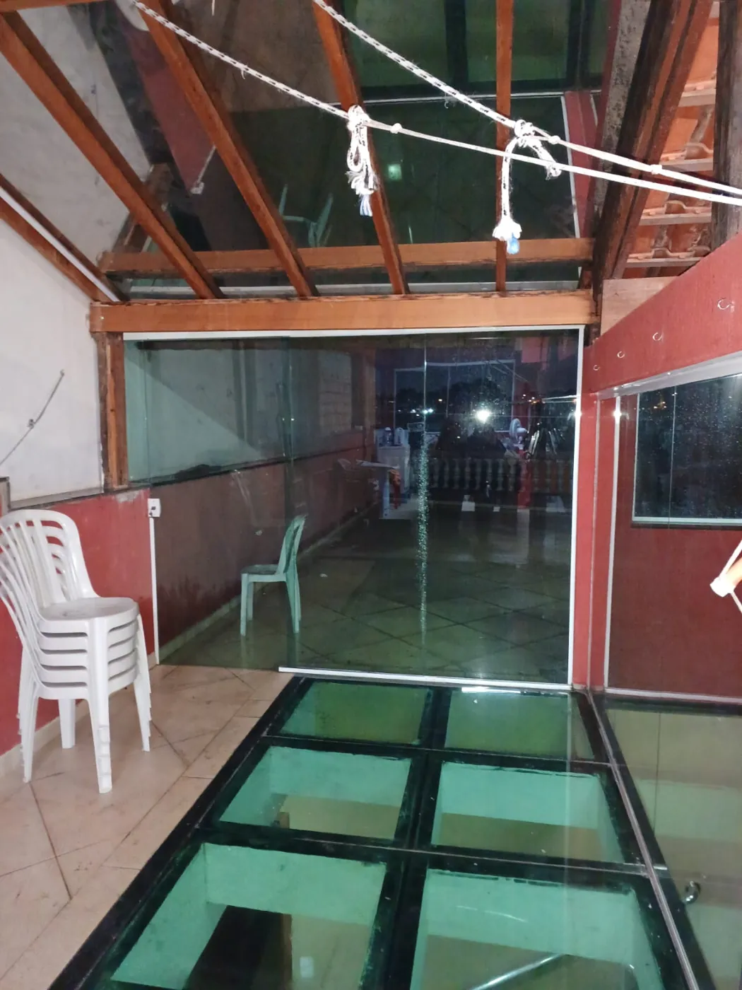 Área com piso de placas de vidro e fechamento lateral em vidro sob cobertura de madeira