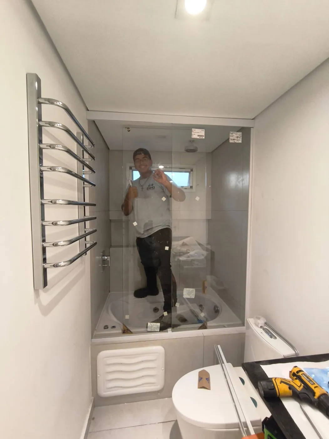 Box de vidro instalado sobre banheira, com profissional da Êxito ao fundo