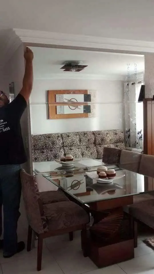 Profissional da Êxito instalando espelho de parede atrás de mesa de jantar com tampo de vidro