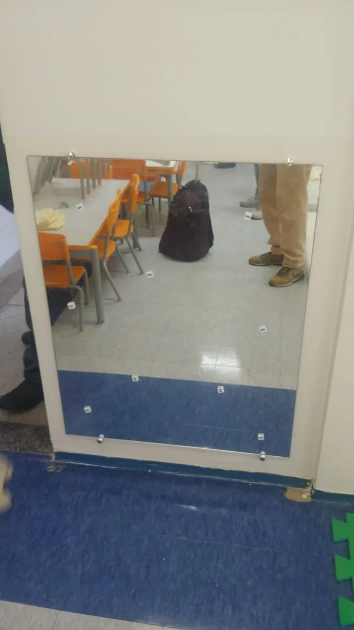 Espelho fixado com botões em parede de refeitório com mesas e cadeiras laranja