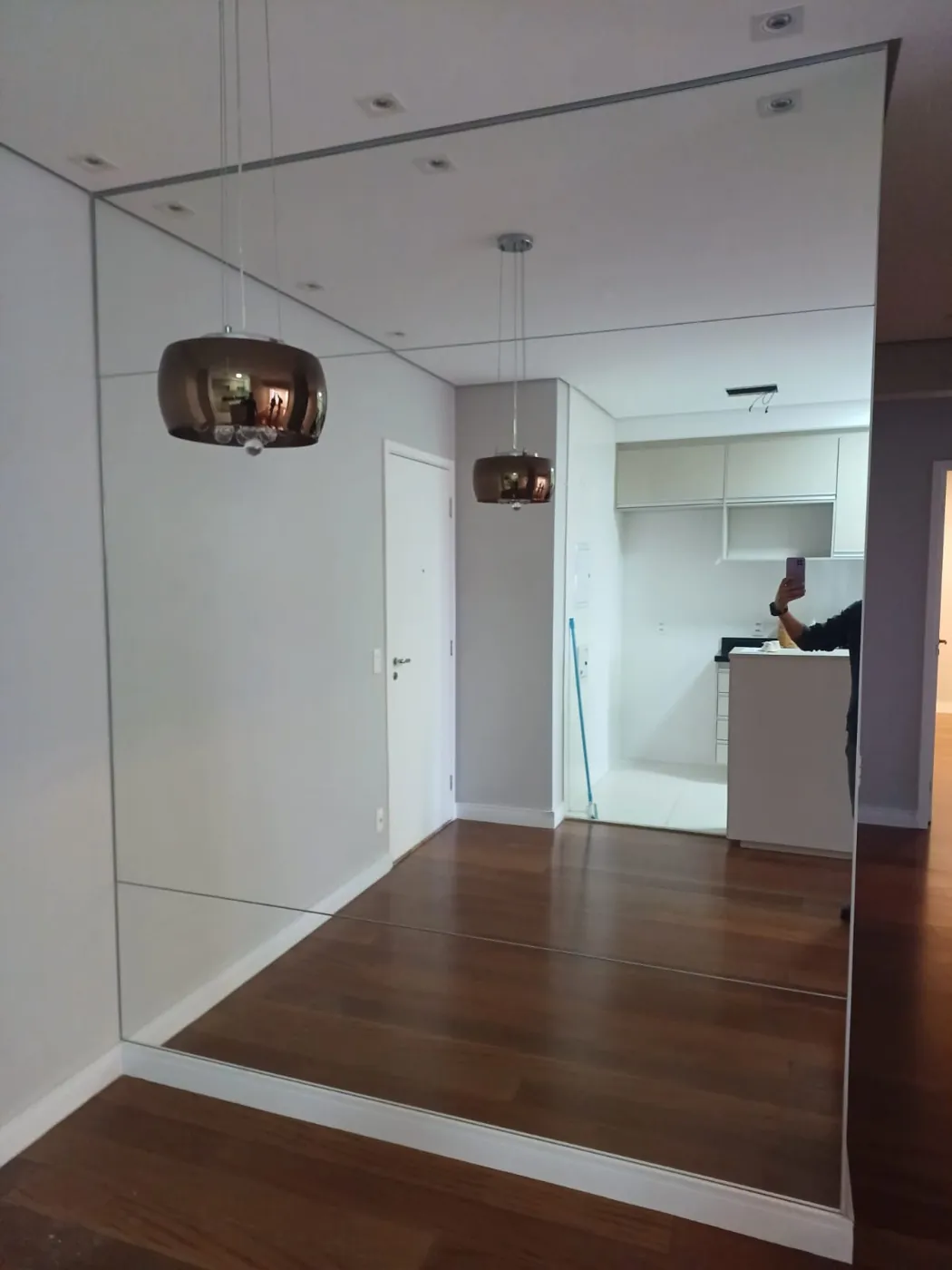 Parede inteira espelhada em sala com piso de madeira e pendentes cobre