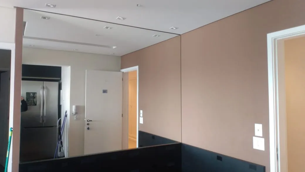 Espelho cobrindo parede inteira, refletindo a cozinha e as portas do apartamento
