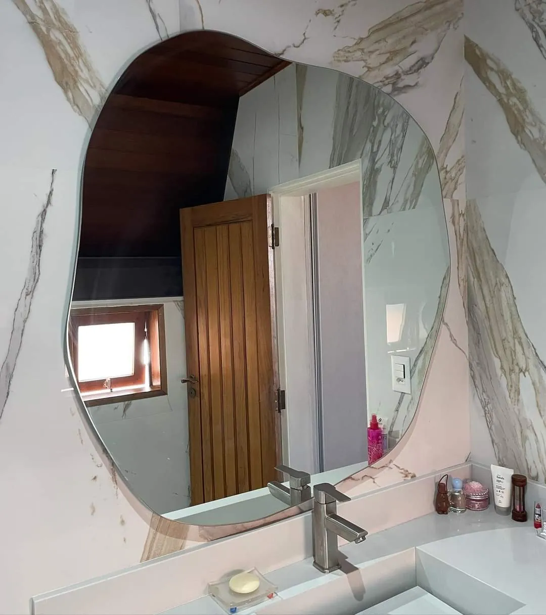 Espelho de formato orgânico instalado sobre bancada de lavabo com revestimento marmorizado