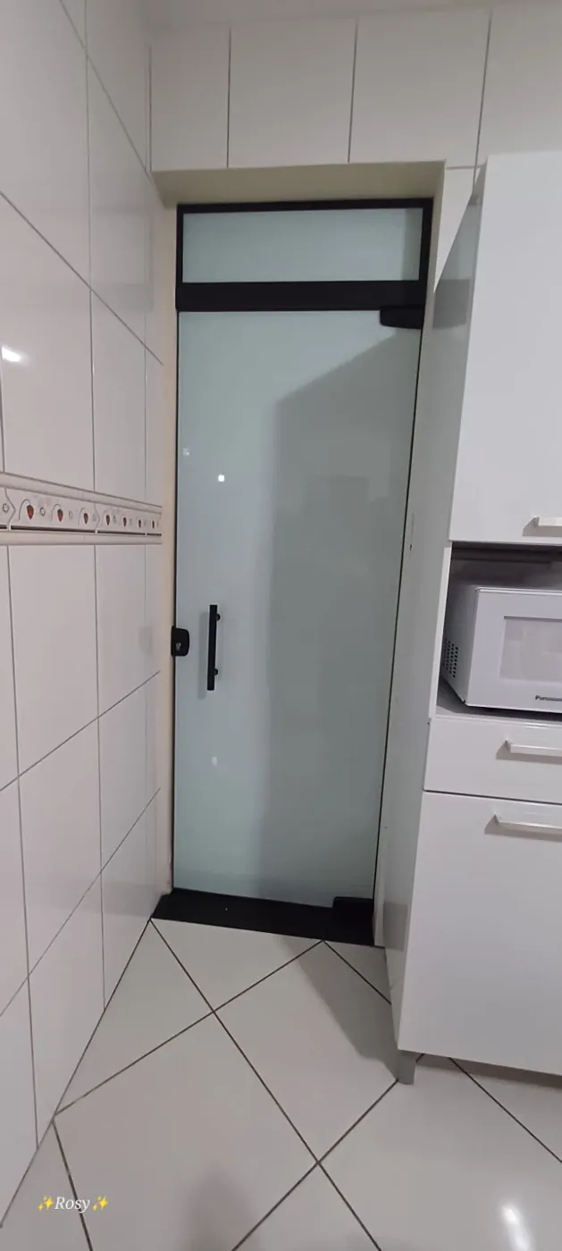 Porta de vidro jateado com perfis pretos e bandeira superior em área de serviço