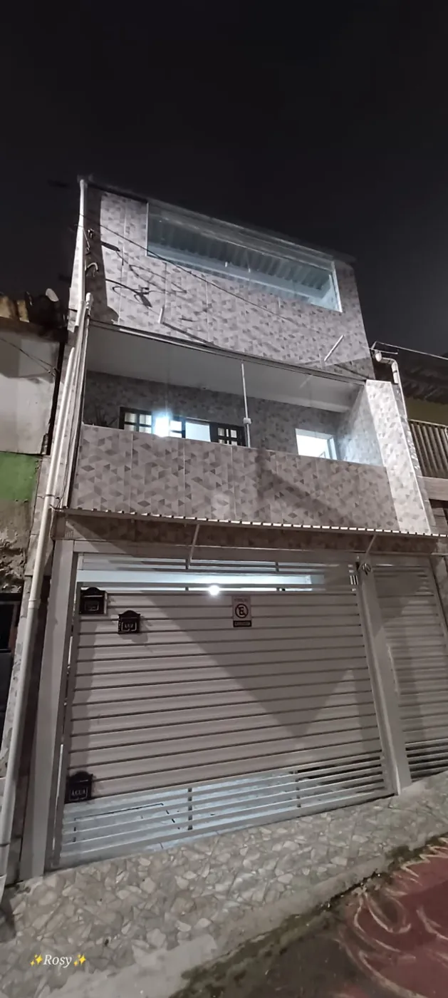 Fachada de sobrado à noite com elementos de vidro na varanda e no último pavimento