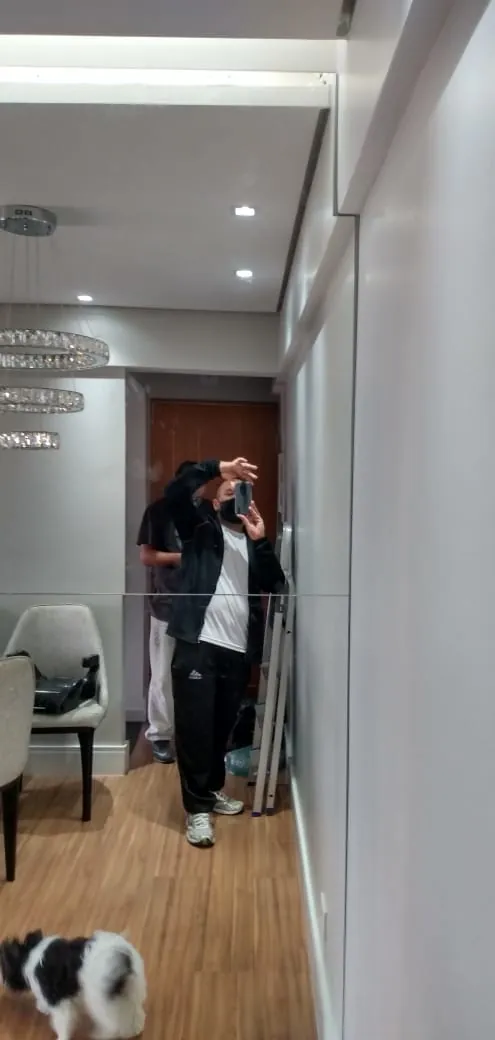 Parede revestida com espelho em sala, refletindo o corredor e a iluminação do ambiente