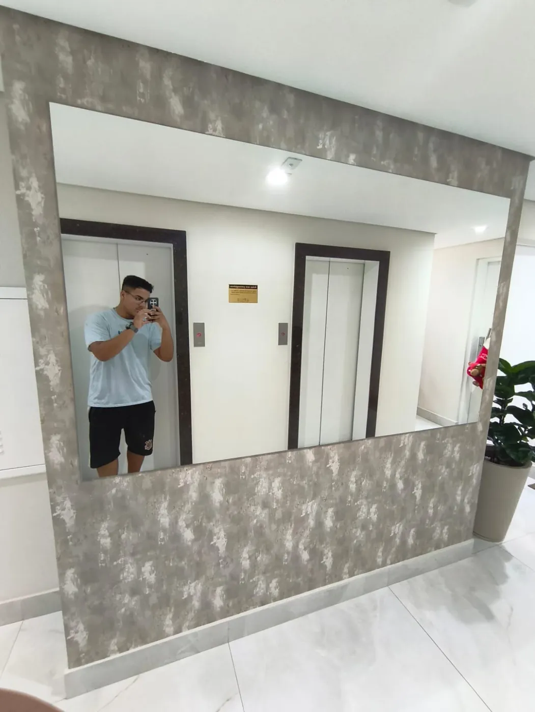 Espelho retangular instalado em parede com revestimento texturizado em hall de elevadores